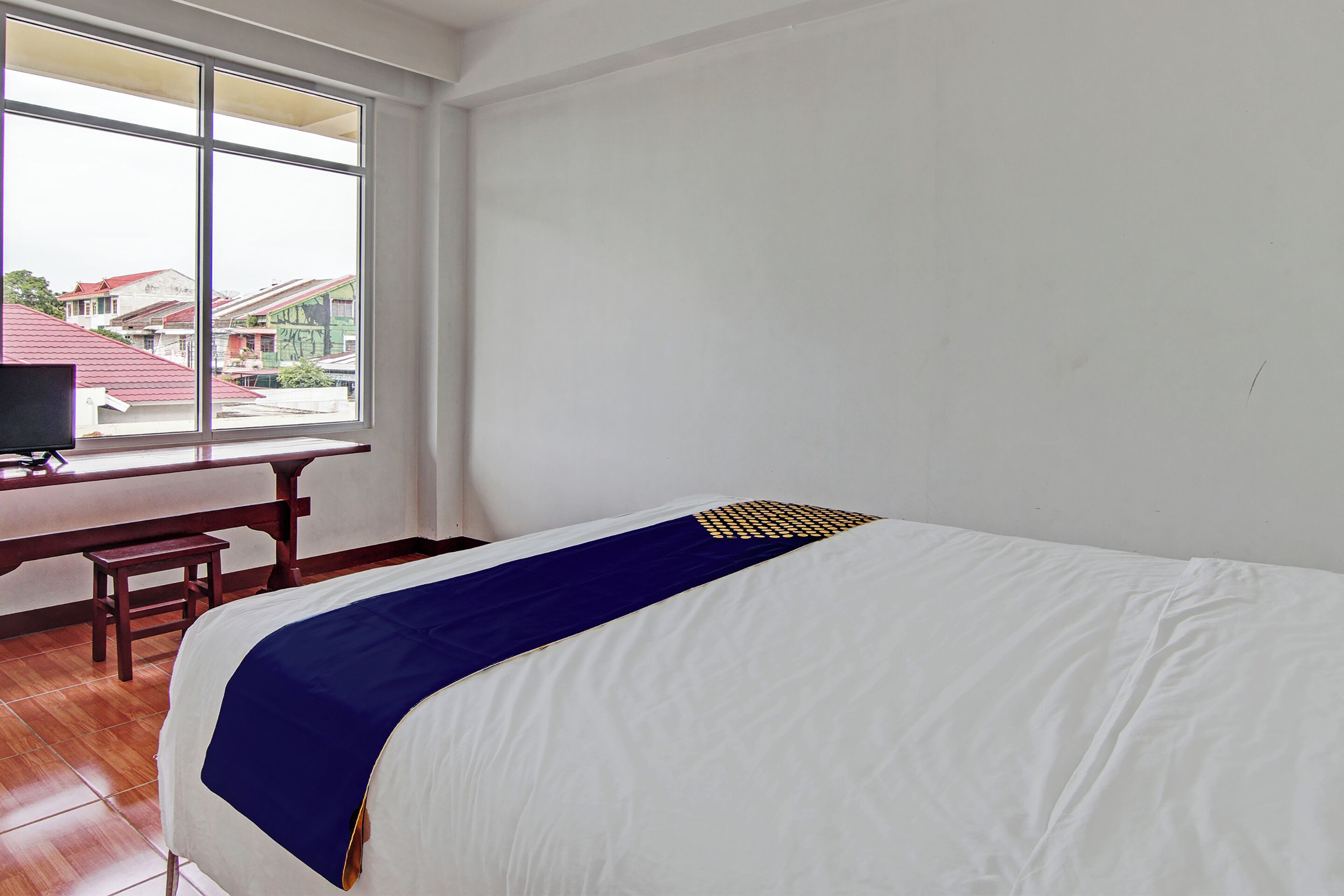 A hotel room with a bed, a desk, and a window with a view of buildings.