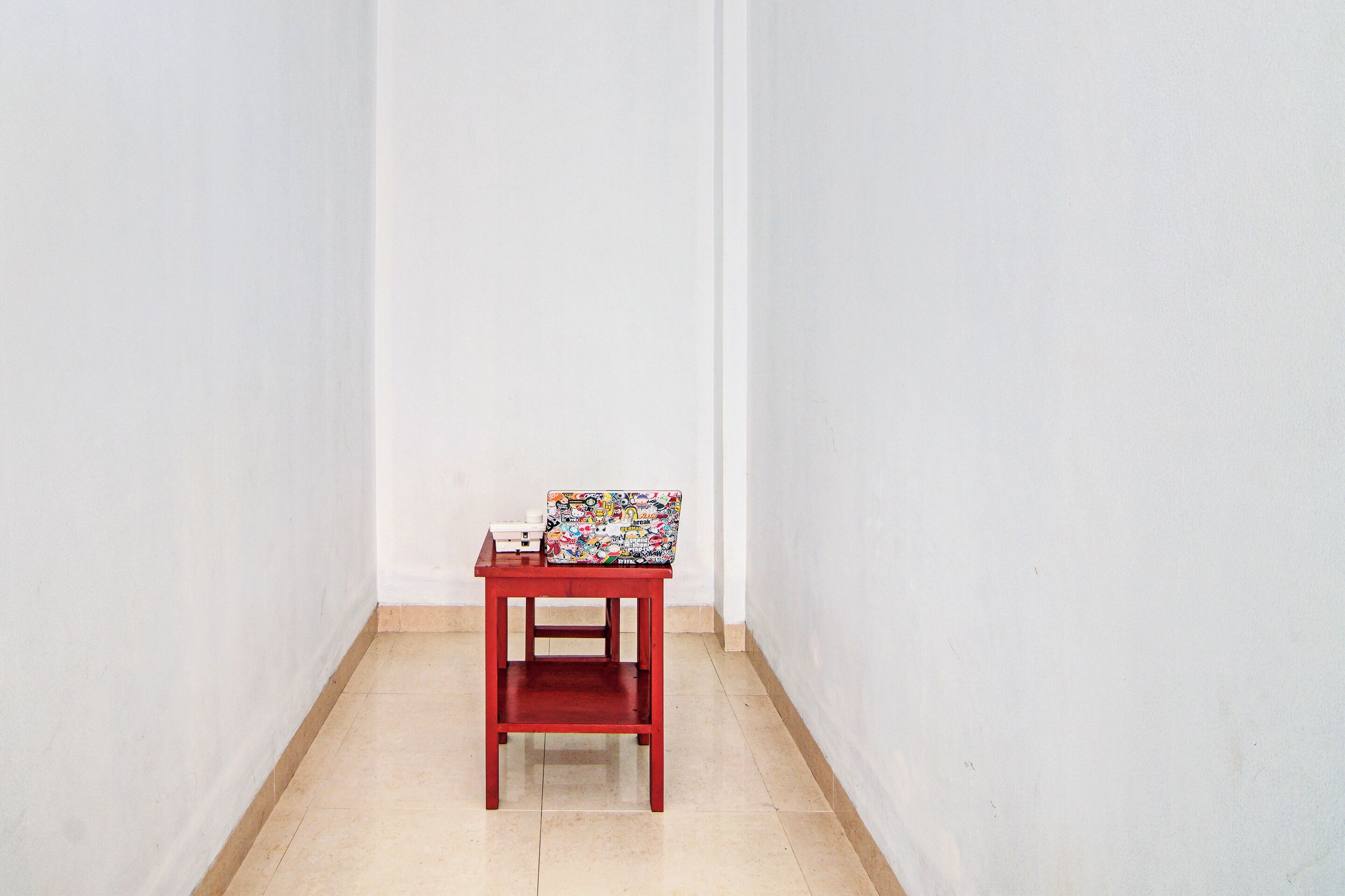 A small red table with a colorful object on top, located in a narrow hallway with white walls and a tiled floor.
