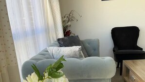 Uma sala de estar com um sofá azul claro, uma poltrona preta, uma mesinha de madeira e um quadro com uma paisagem florestal na parede.