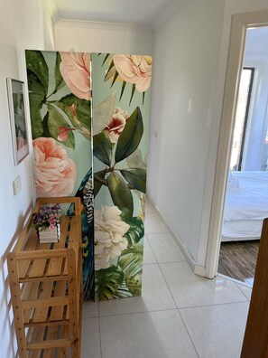 A hallway with a floral-patterned sliding door, a wooden bench with books and flowers, and a bed visible through an open door. - Close Airport Style Home (Dallas)