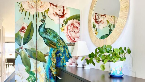 Uma casa de banho moderna com uma toucador de madeira escura, um espelho, uma planta em vaso e um quadro decorativo de pavão.
