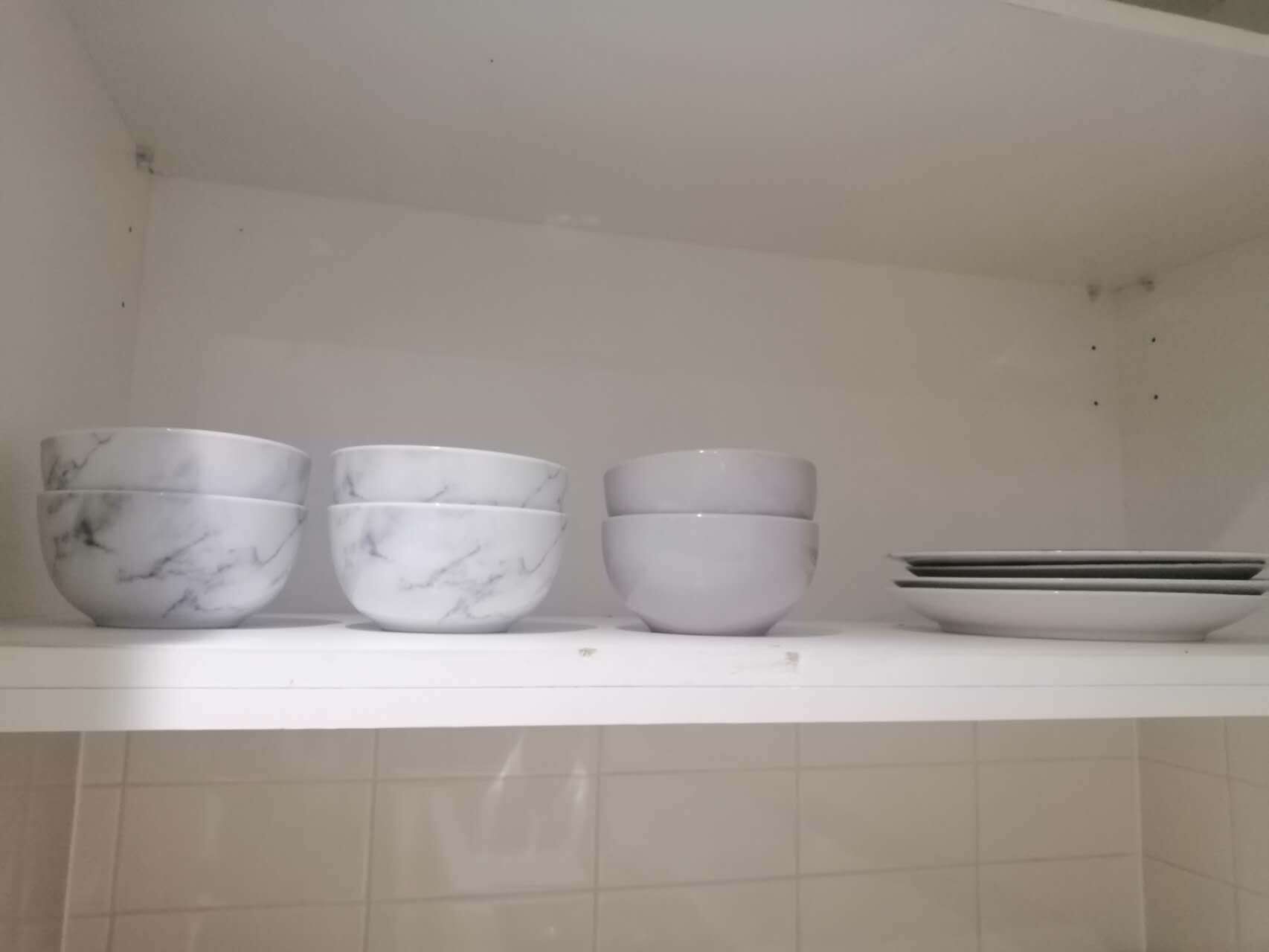 Una repisa de cocina con tres cuencos de mármol blanco y una pila de platos blancos.