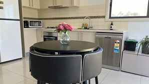 Uma cozinha moderna com uma mesa de jantar redonda, cadeiras pretas, um vaso com flores e uma janela que oferece luz natural.