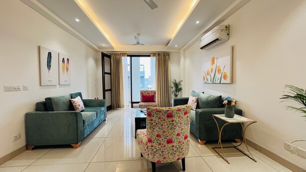A modern living room with two sofas, a floral armchair, a small table, and artwork on the walls. - BluO 3BHK Golf Course Road Balcony Lift  (Gurugram)