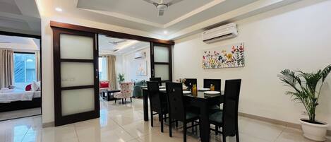A hotel room with a dining area, a ceiling fan, an air conditioning unit, and a potted plant.