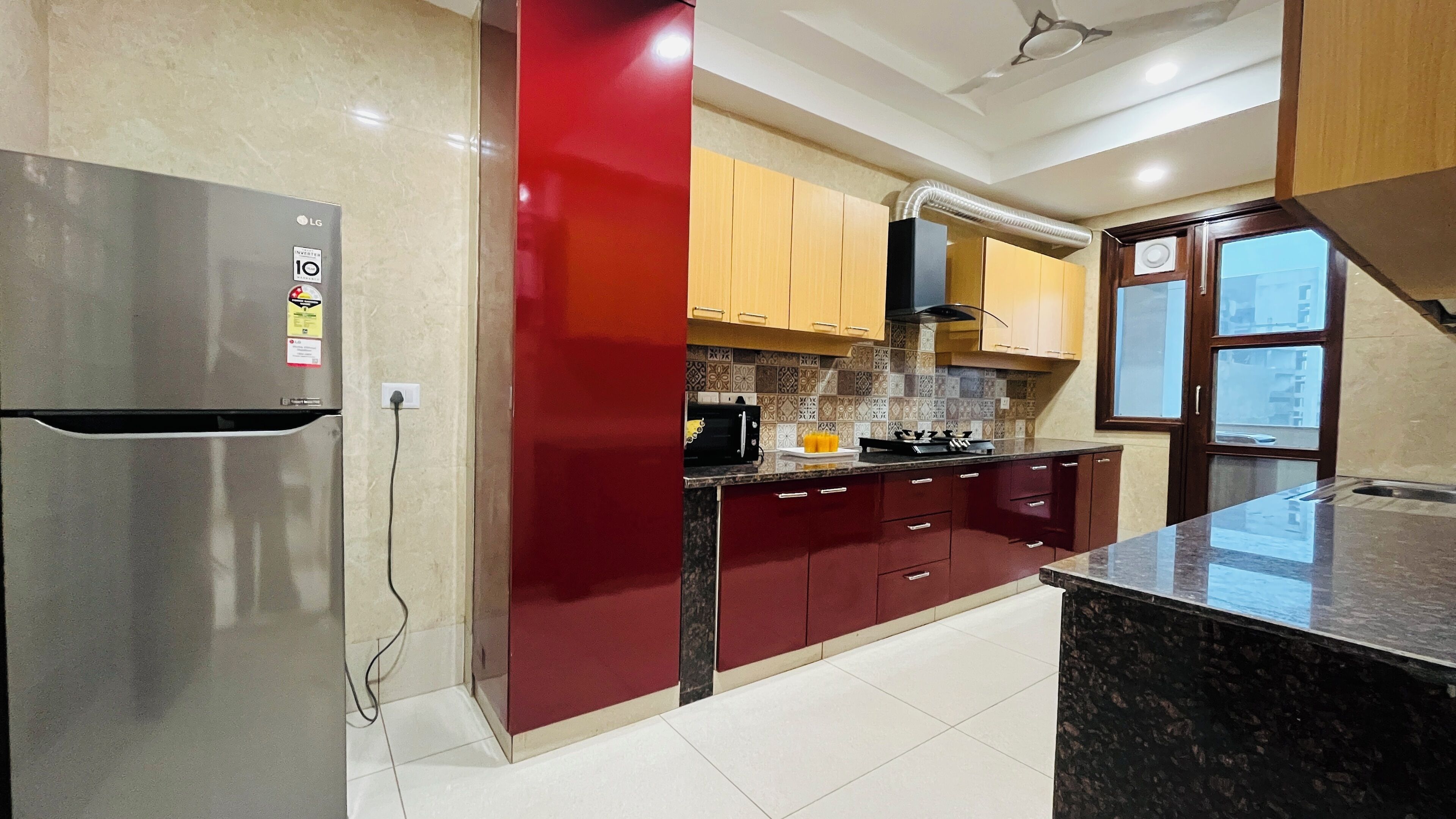 A modern kitchen with a stainless steel refrigerator, red cabinets, and a tiled backsplash.