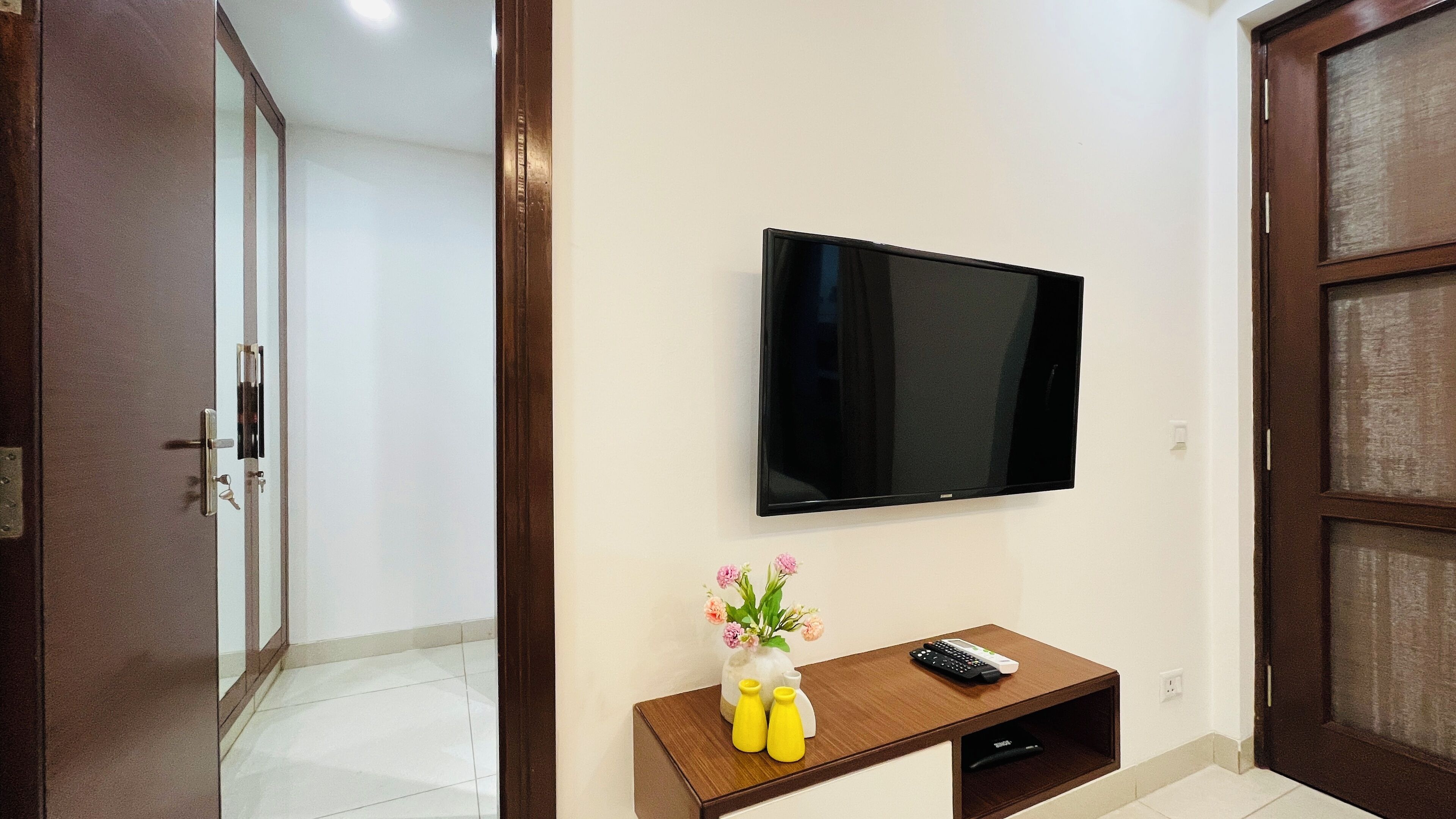 A room with a mounted TV, a wooden console table with a vase of flowers, and a door.