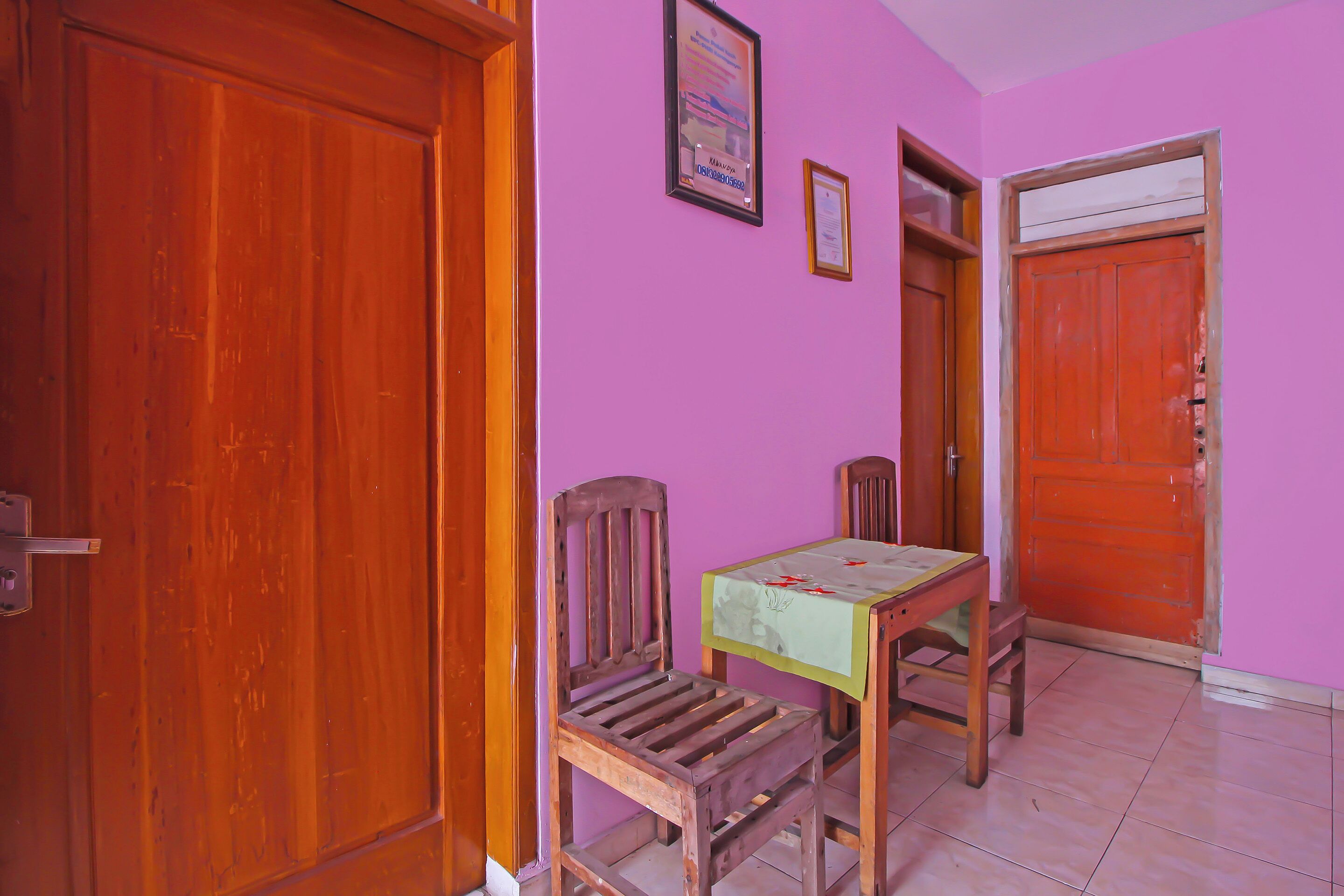 A room with a wooden door, a wooden chair, a small table with a green tablecloth, and a pink wall.