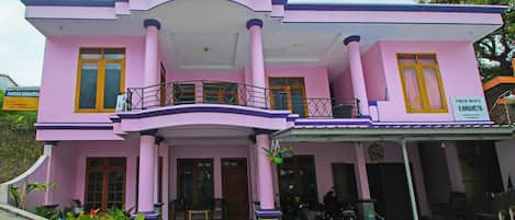 A pink building with a balcony, columns, and a sign indicating it is a place for lodging.