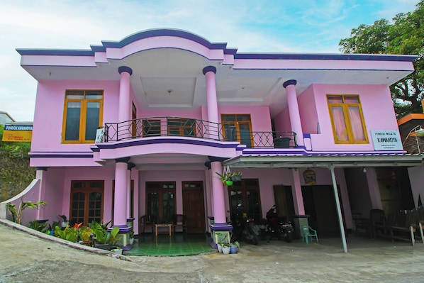 A pink building with a balcony, columns, and a sign indicating it is a place for lodging.