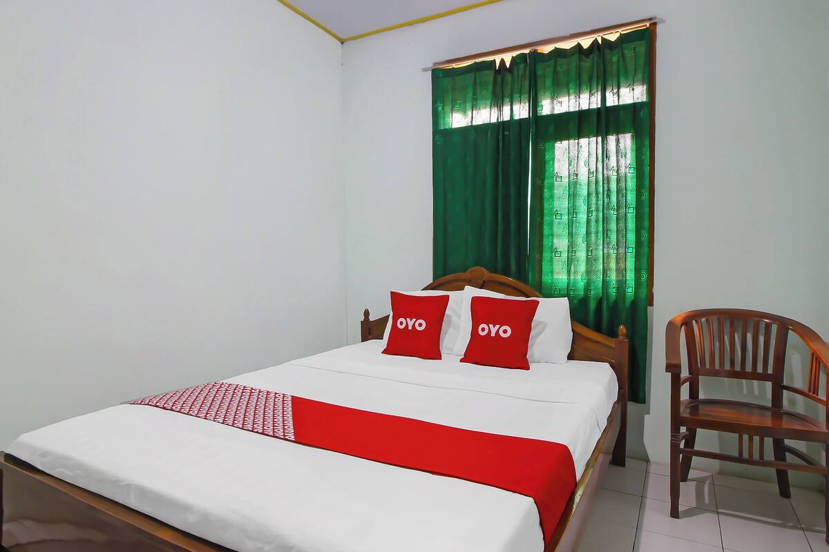 A neatly made bed with a red and white bedspread, two red pillows with "OYO" on them, and a green curtain partially covering a window.