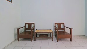 Um quarto com um banco de madeira e duas cadeiras, uma mesinha e uma parede branca lisa.