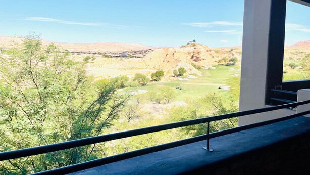 Blick von einem Balkon auf einen Golfplatz bei blauem Himmel.