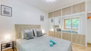 Ein Schlafzimmer mit einem Bett, Nachttischen, einem großen Spiegel und einem Fenster.