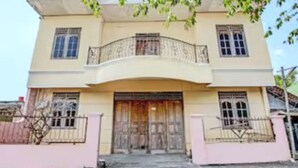 Un edificio de dos pisos con un balcón, una puerta de madera grande y una pared rosa.