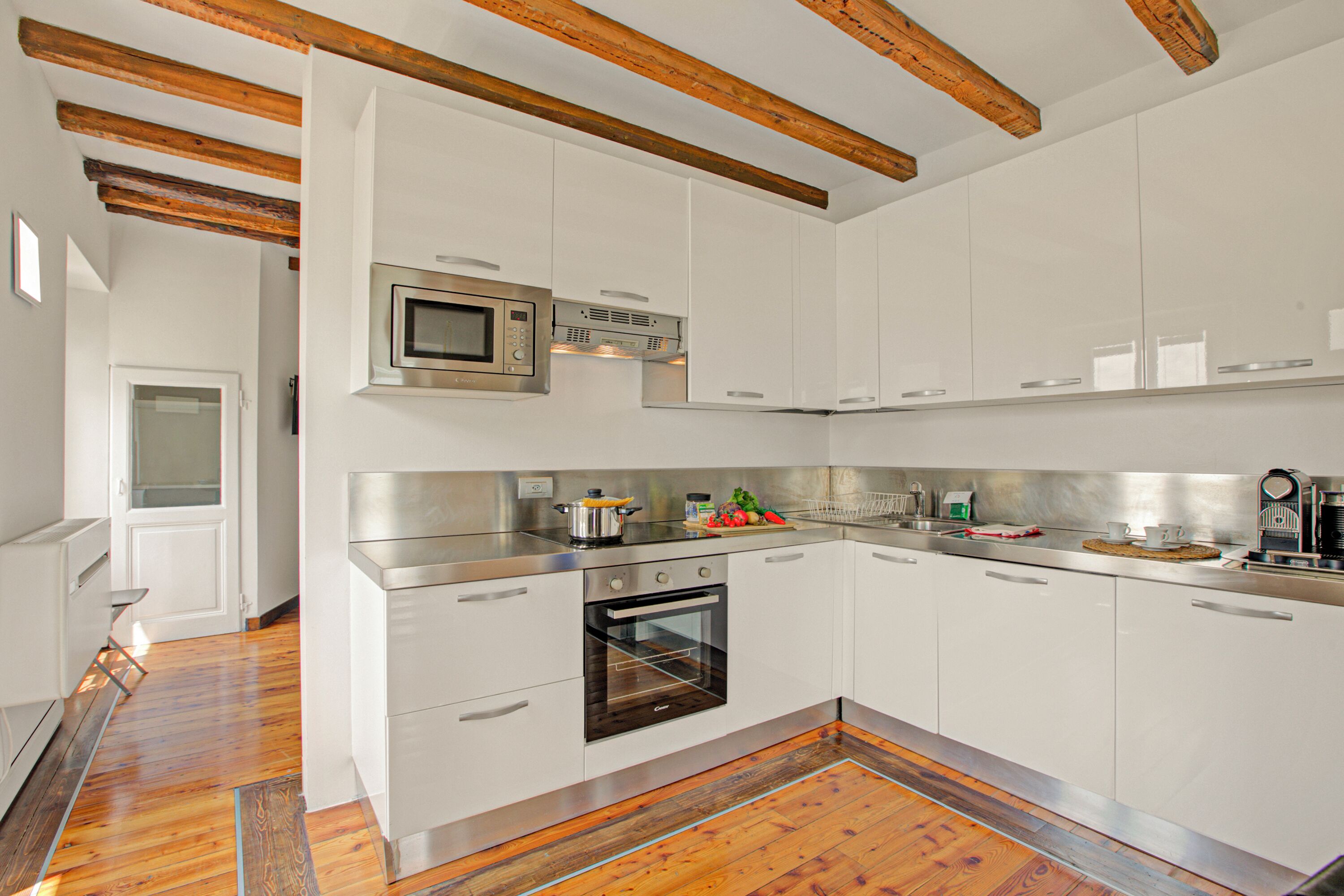 A modern kitchen with white cabinets, stainless steel appliances, and wooden beams on the ceiling.