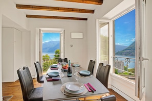 Uma área de refeições com mesa posta para quatro, vista para um lago e montanhas, e varanda com corrimão.
