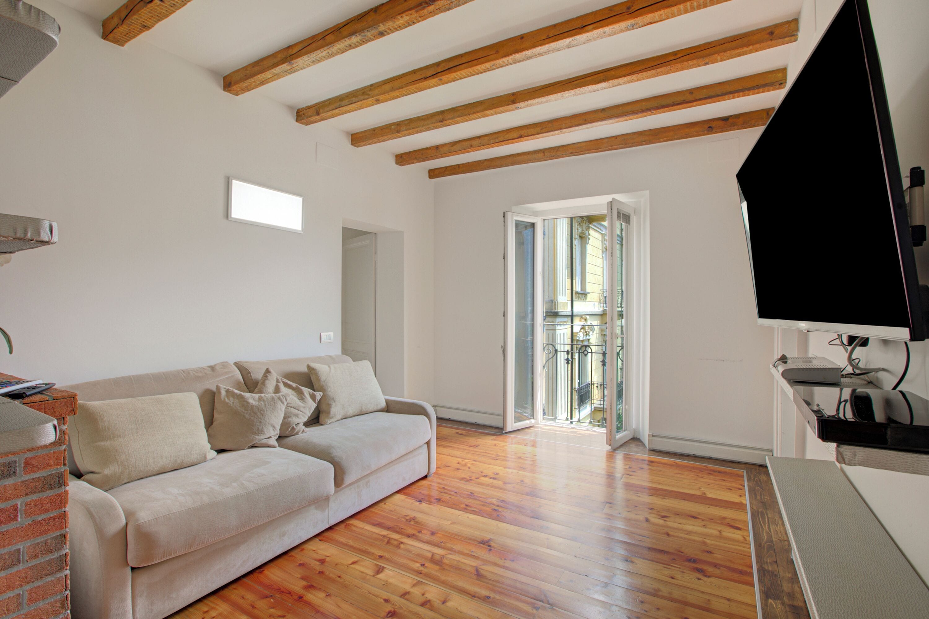 A living room with a wooden floor, a sofa, a TV, and a balcony door.