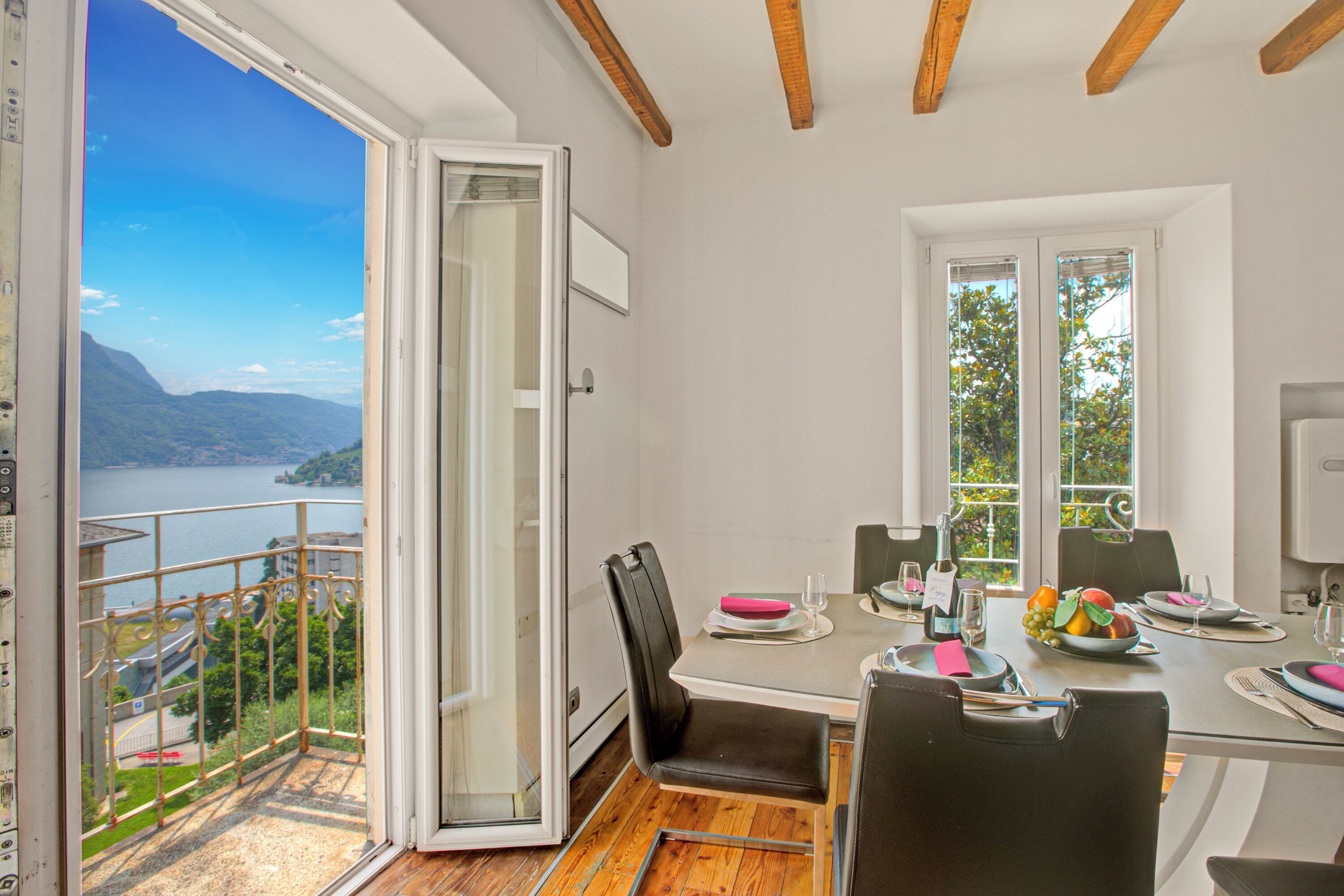 Un coin repas avec une table dressée pour quatre personnes, une vue sur un lac et un balcon doté d’une balustrade.