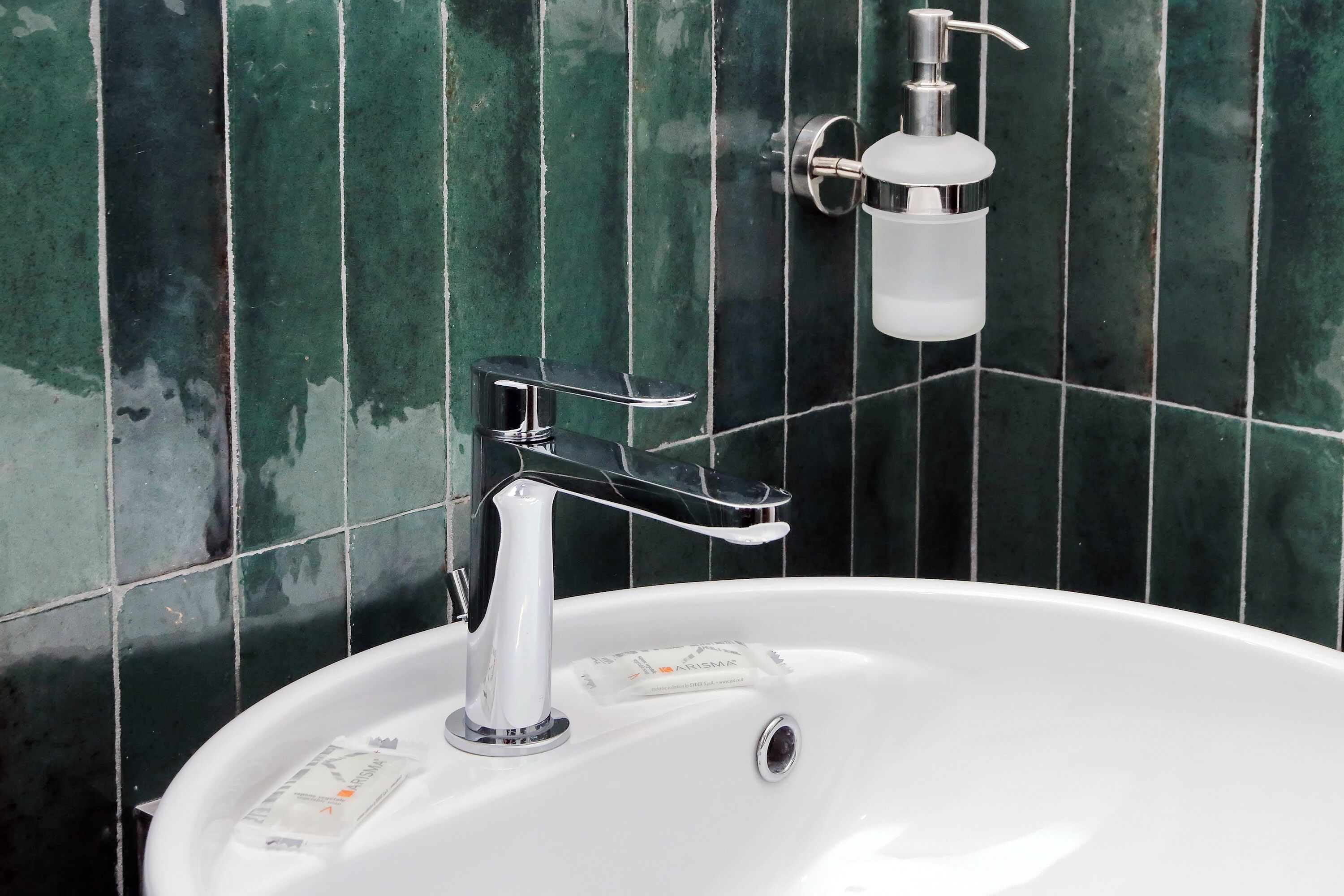 A bathroom with a white sink, chrome faucet, and soap dispenser.