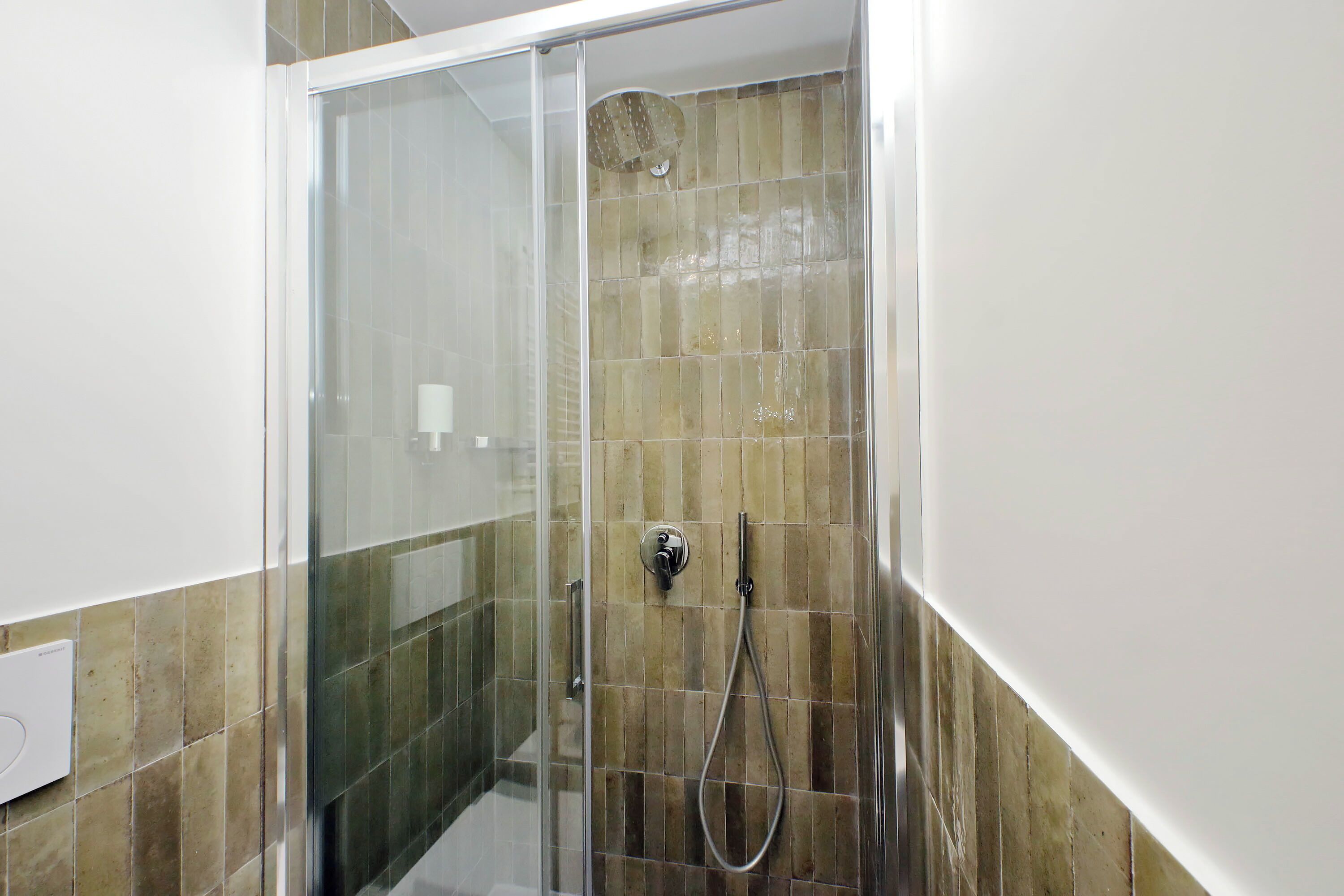 A glass-enclosed shower with a handheld showerhead and a wall-mounted faucet.
