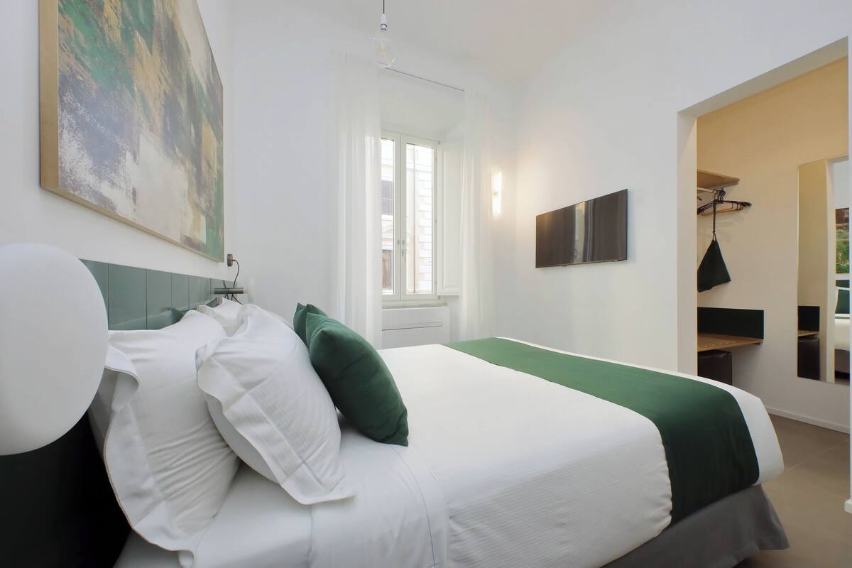 A hotel room with a large bed, a flat-screen TV, a painting on the wall, and a window with curtains.