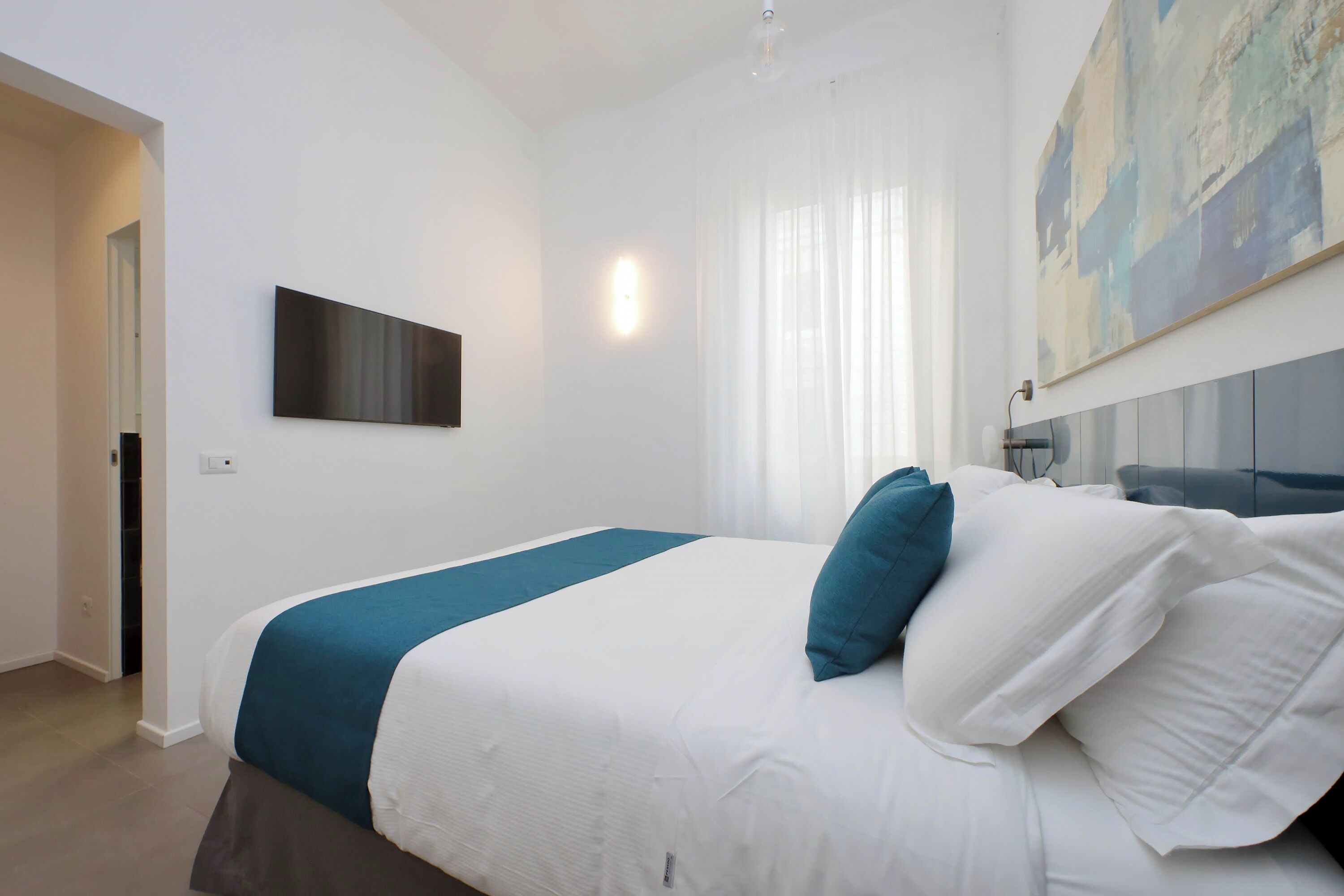 Ein modernes Hotelzimmer mit einem großen Bett, einem flachbildfernseher an der Wand und einem Gemälde über dem Bett.