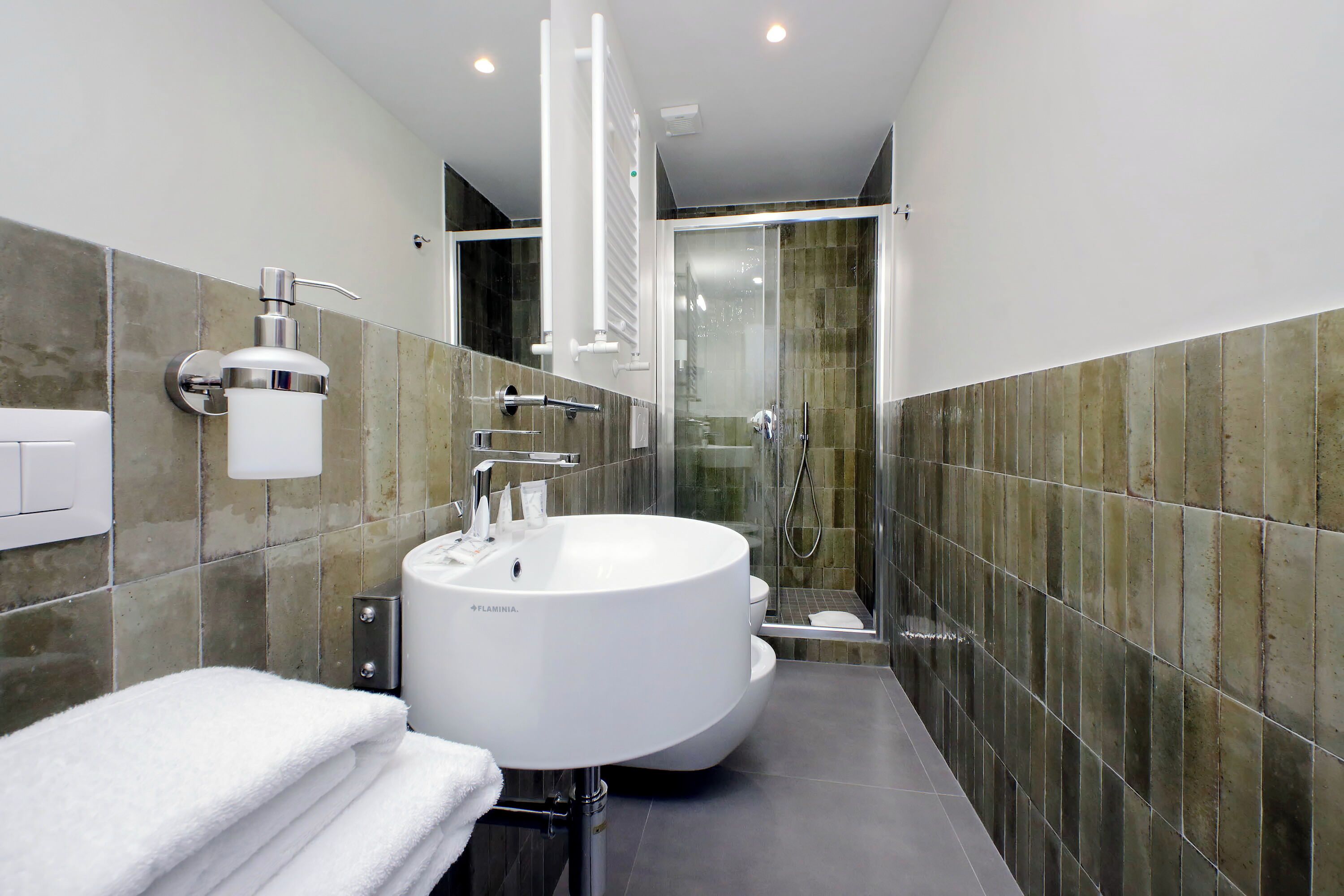 A modern bathroom with a large white sink, a glass shower enclosure, and a towel rack.