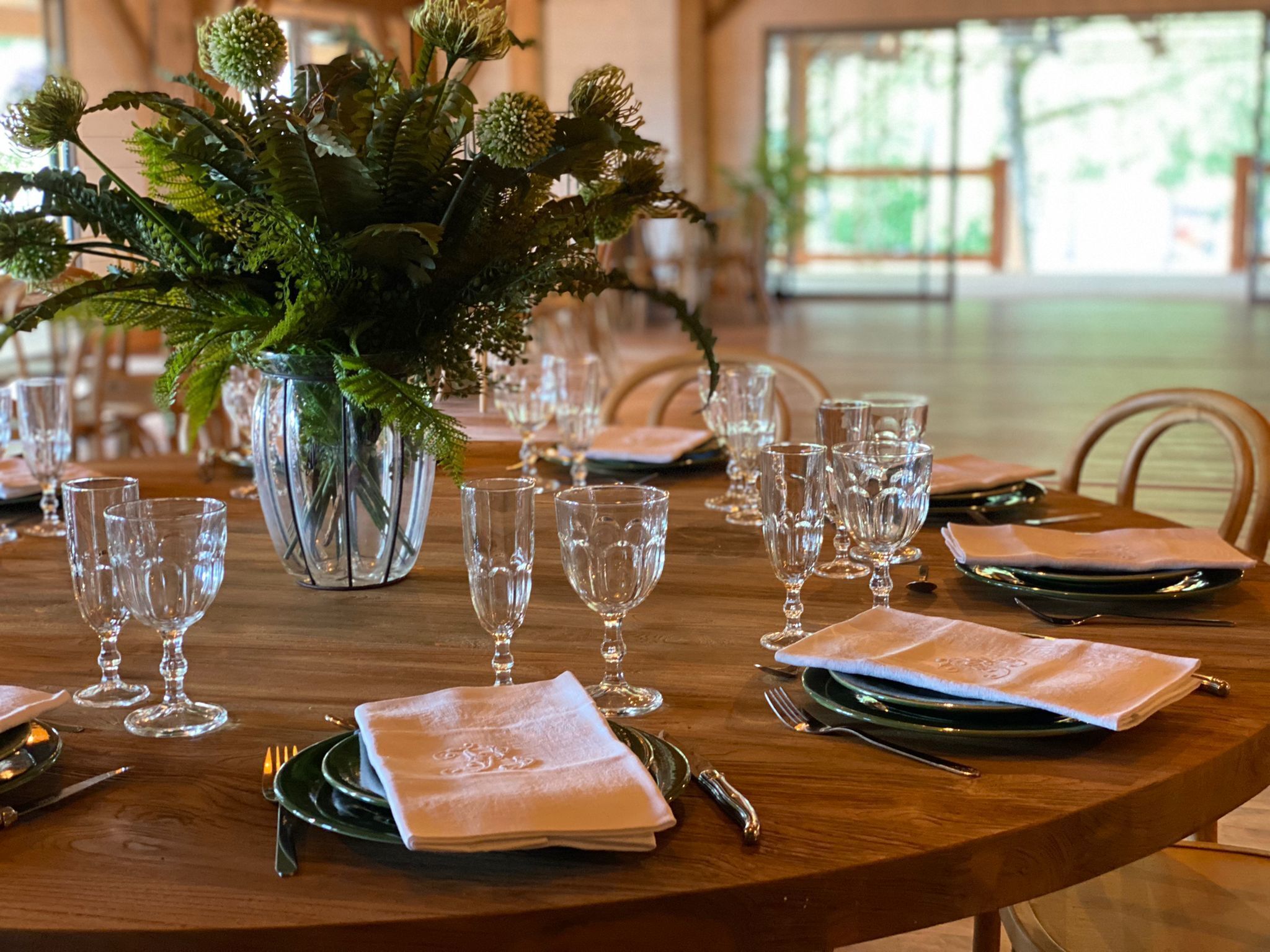 Una mesa de comedor dispuesta con cubertería de vidrio transparente, platos verdes y servilletas blancas.