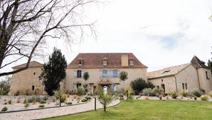A stone building with a tiled roof, multiple windows, and a well-maintained garden with various plants and a gravel path. - Villa Biloba (Beaumontois-en-Périgord)