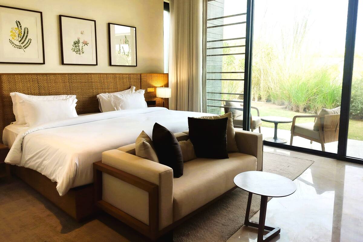 Ein Hotelzimmer mit einem großen Bett, einer Sitzecke, einem kleinen Tisch und Blick ins Grüne.