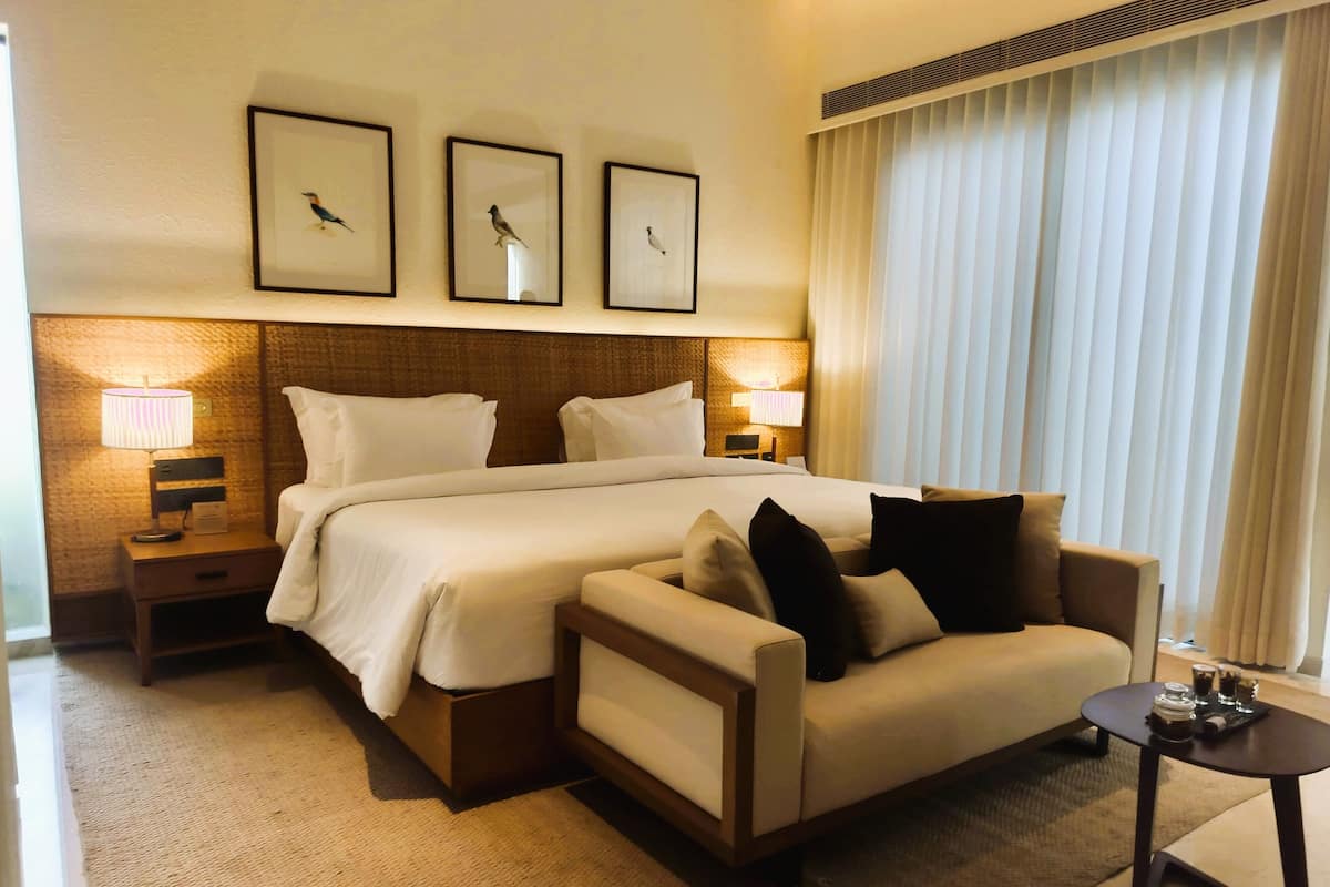 Ein Hotelzimmer mit einem großen Bett, einem Schlafsofa, einem kleinen Tisch mit Lampe sowie drei gerahmten Bildern an der Wand.