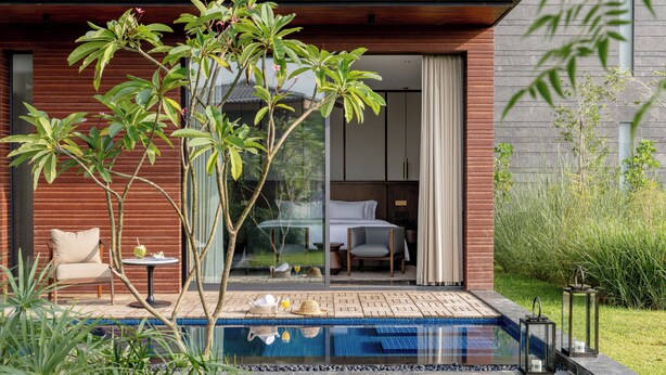 A modern outdoor pool area with a glass-enclosed room, a lounge chair, and a small table with a drink. - MYSA Zinc Journey by The Fern (A Glade One Golf Resort) Nani Devati, Gujarat  (Sanand)