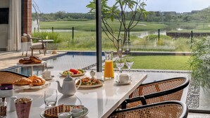 A breakfast table with croissants, waffles, and fruit, overlooking a golf course and water. - MYSA Zinc Journey by The Fern (A Glade One Golf Resort) Nani Devati, Gujarat  (Sanand)