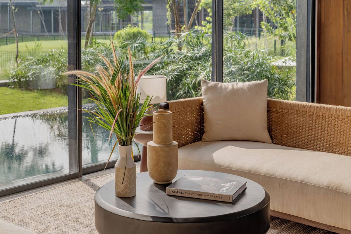 Ein modernes Wohnzimmer mit einer Couch, einem runden Couchtisch und Blick auf einen Garten durch große Fenster.