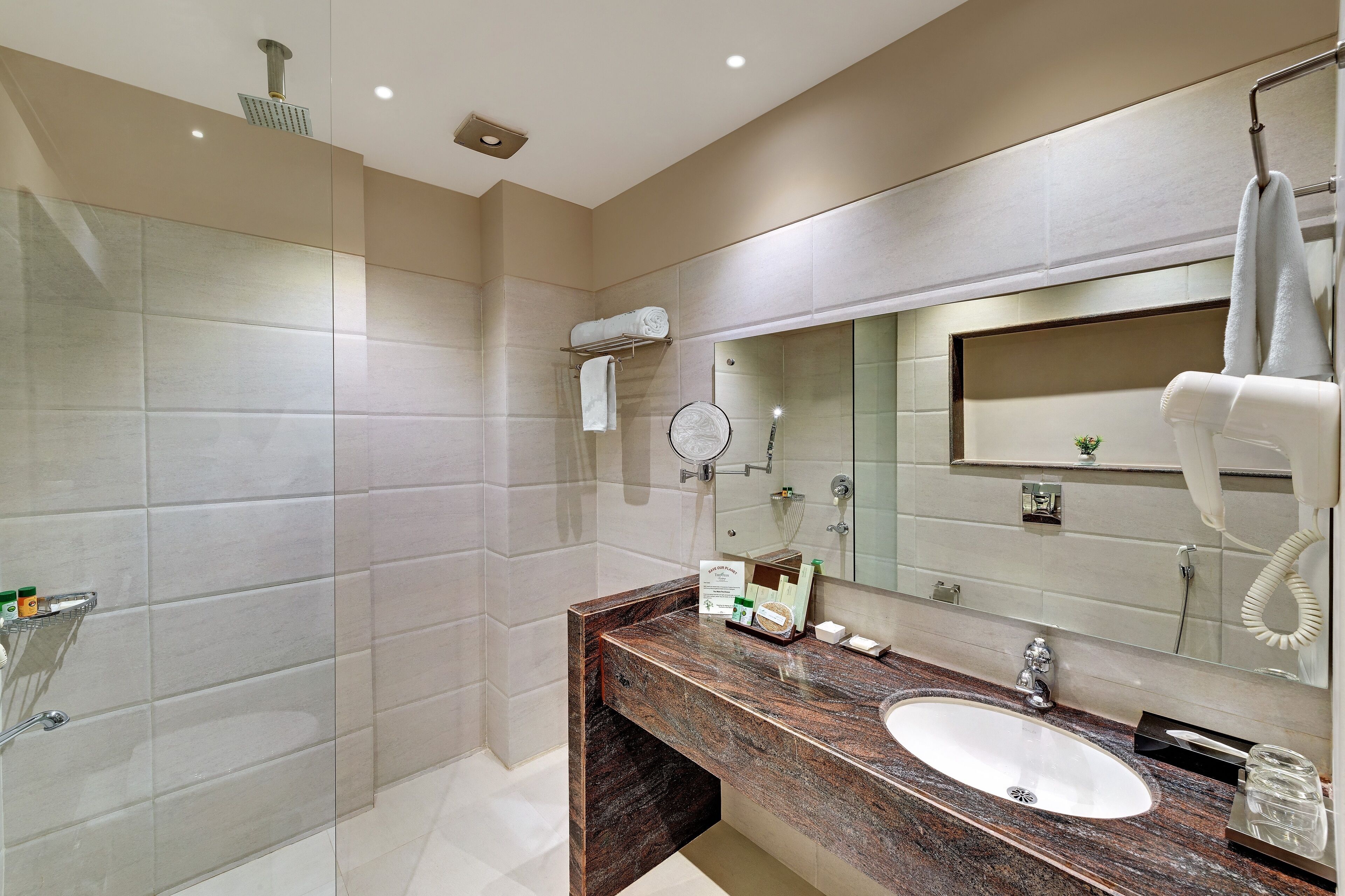 A modern bathroom with a marble sink, a large mirror, a handheld showerhead, and a towel rack.