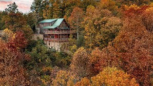 A log cabin with a green roof, surrounded by autumn foliage. - 180 Mtn Views! Pool&Pond Access! Sleep 16! Hot tub! Firepit! Prime Location! (Sevierville)