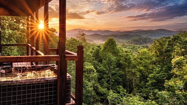 A wooden deck with a view of a forested landscape and a sunset. - 180 Mtn Views! Pool&Pond Access! Sleep 16! Hot tub! Firepit! Prime Location! (Sevierville)