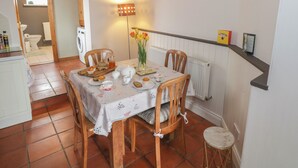 A dining area with a table set for tea, surrounded by chairs, a vase with flowers, and a radiator. - 7 Aikenhead Terrace (Foxford)