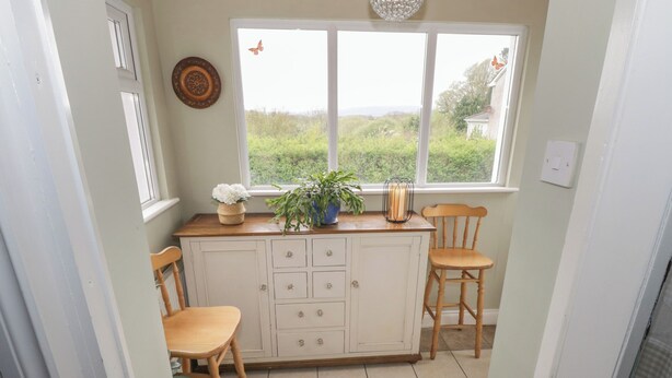 A kitchen with a window, two wooden chairs, a white cabinet, and a potted plant. - 7 Aikenhead Terrace (Foxford)