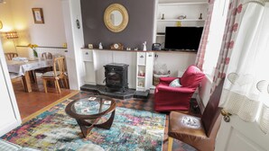 A cozy living room with a fireplace, a dining area, and a colorful rug. - 7 Aikenhead Terrace (Foxford)