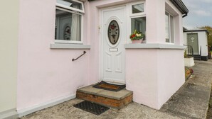 A pink house with a white door, a small porch, and a flower pot on the window sill. - 7 Aikenhead Terrace (Foxford)