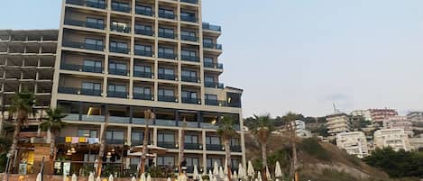 A hotel with multiple floors, outdoor seating with umbrellas, and a beachside location.