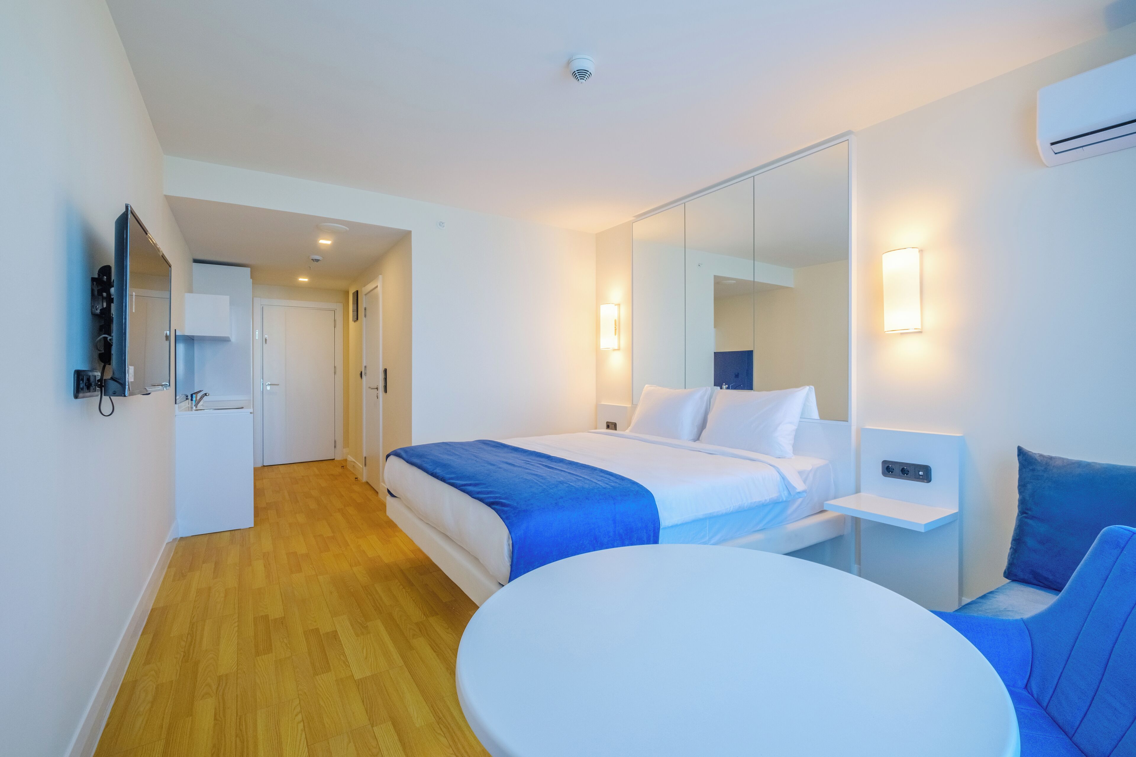 A modern hotel room with a bed, bedside table, and a round table.