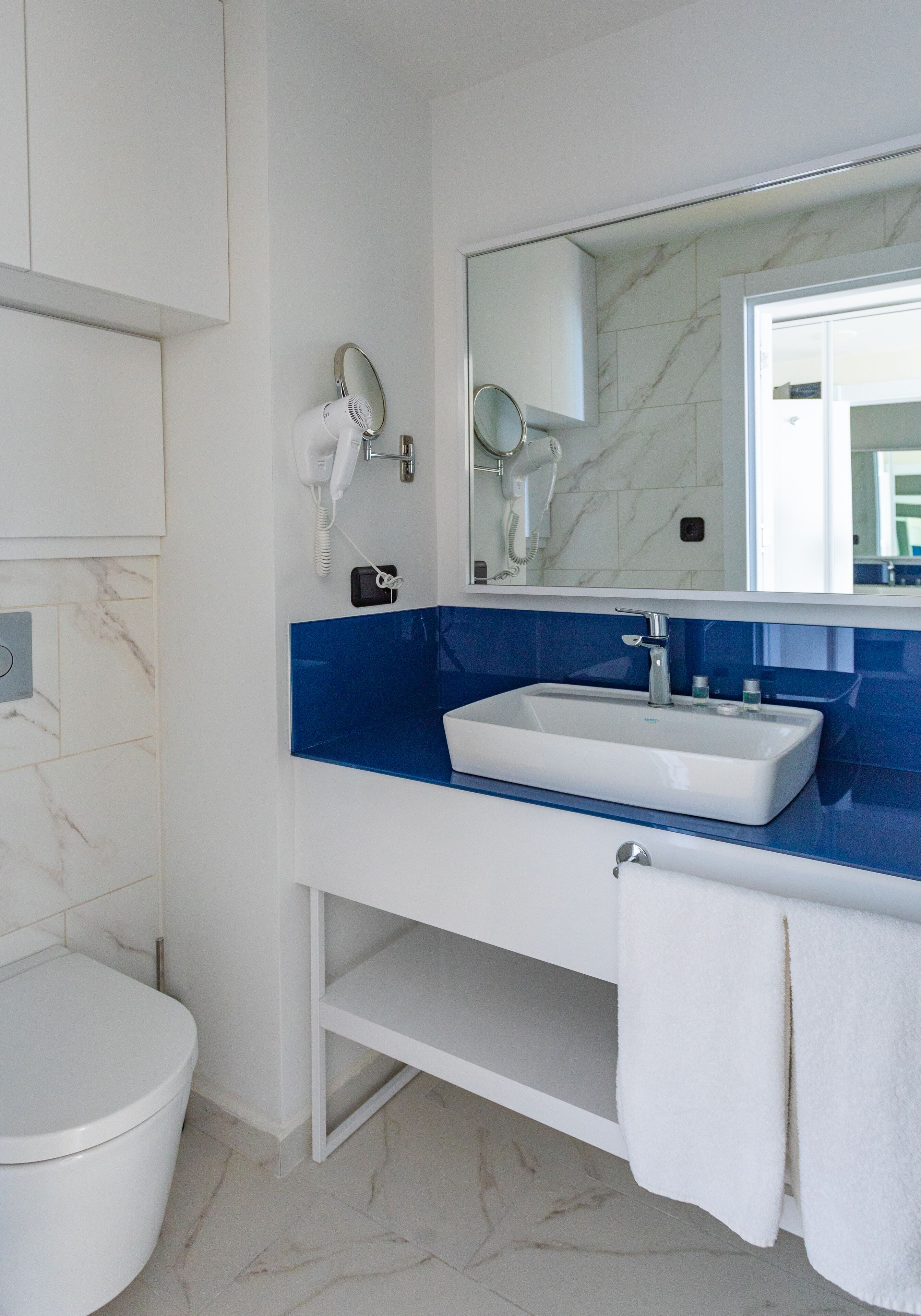 Ein modernes Badezimmer mit einer weißen Toilette, einem blauen Fliesenwaschbecken und einem Spiegel darüber.