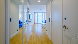 Una habitación de hotel moderna con piso de madera, separador de vidrio, sofá azul y zona de comedor con mesa y sillas.