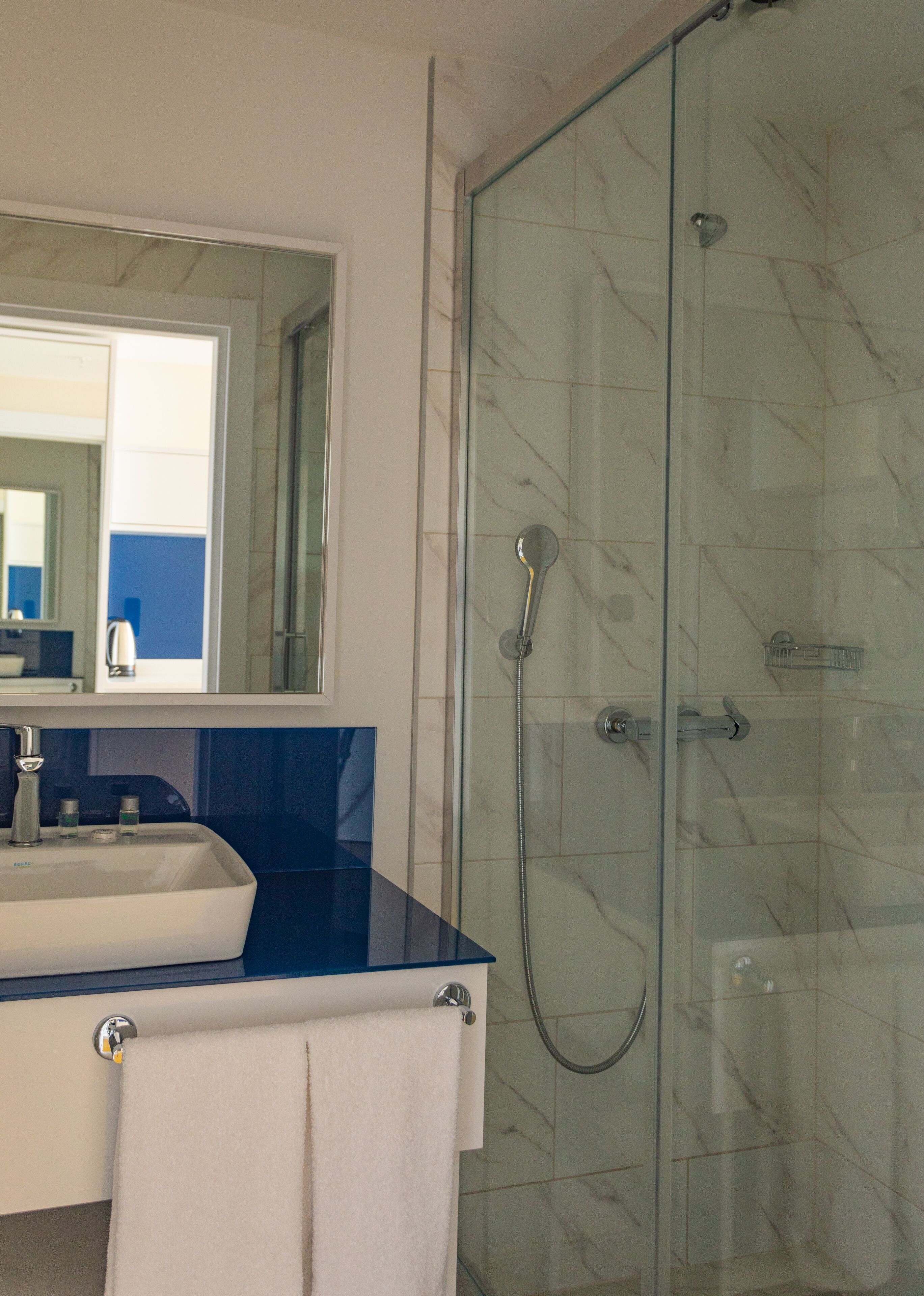 A bathroom with a glass-enclosed shower, a sink with a blue countertop, and a mirror above the sink.