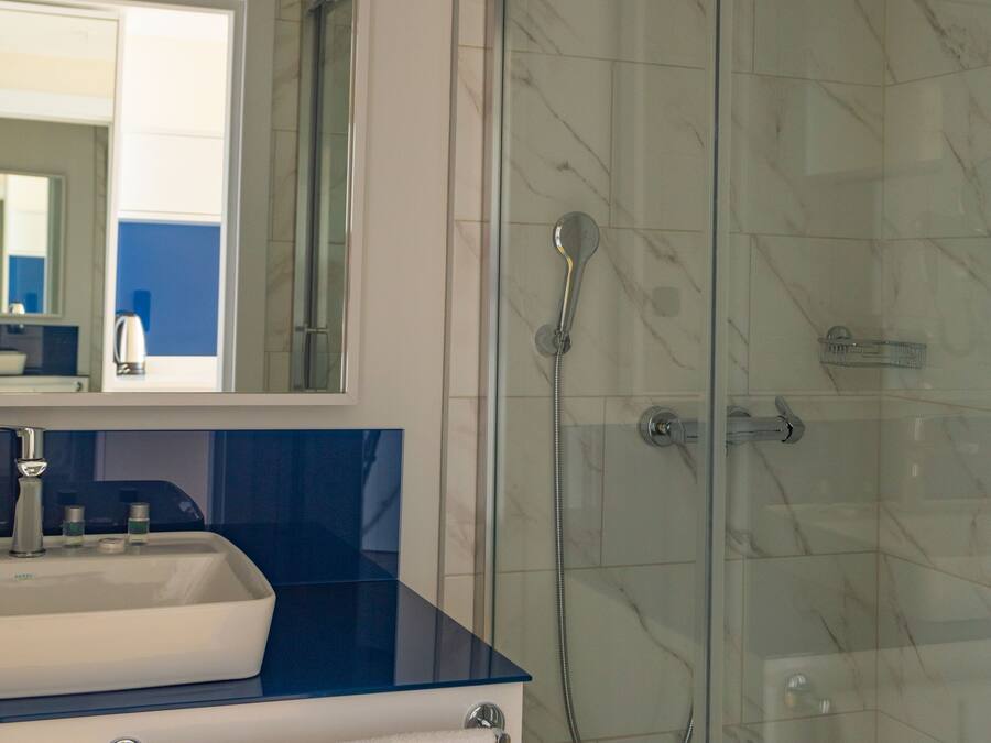 A bathroom with a glass-enclosed shower, a sink with a blue countertop, and a mirror above the sink.