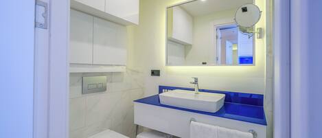Un baño moderno con inodoro blanco, lavamanos con encimera azul y espejo con lupa redonda.