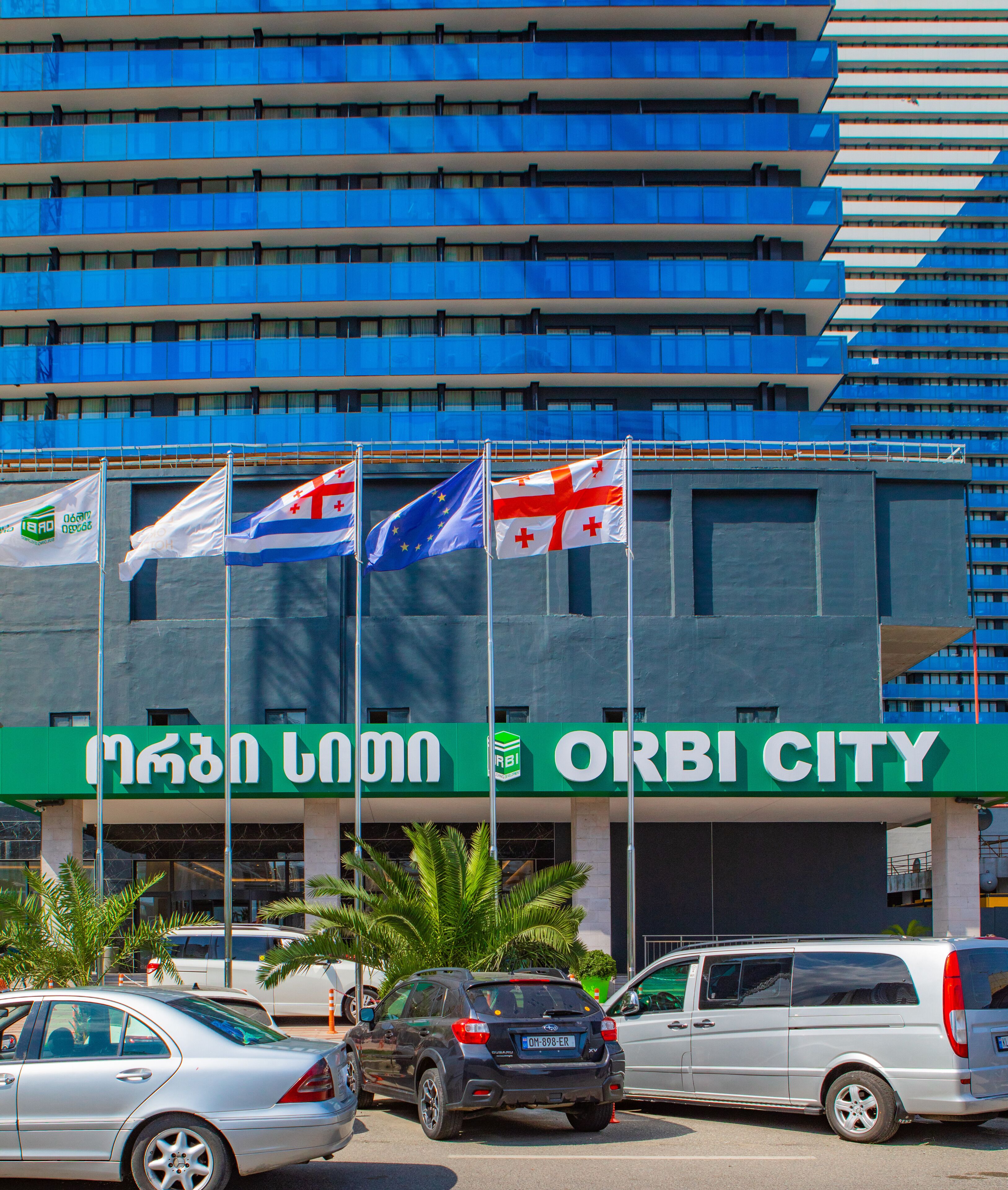 Um edifício moderno com várias bandeiras, incluindo a bandeira da União Europeia, e uma placa com a inscrição 